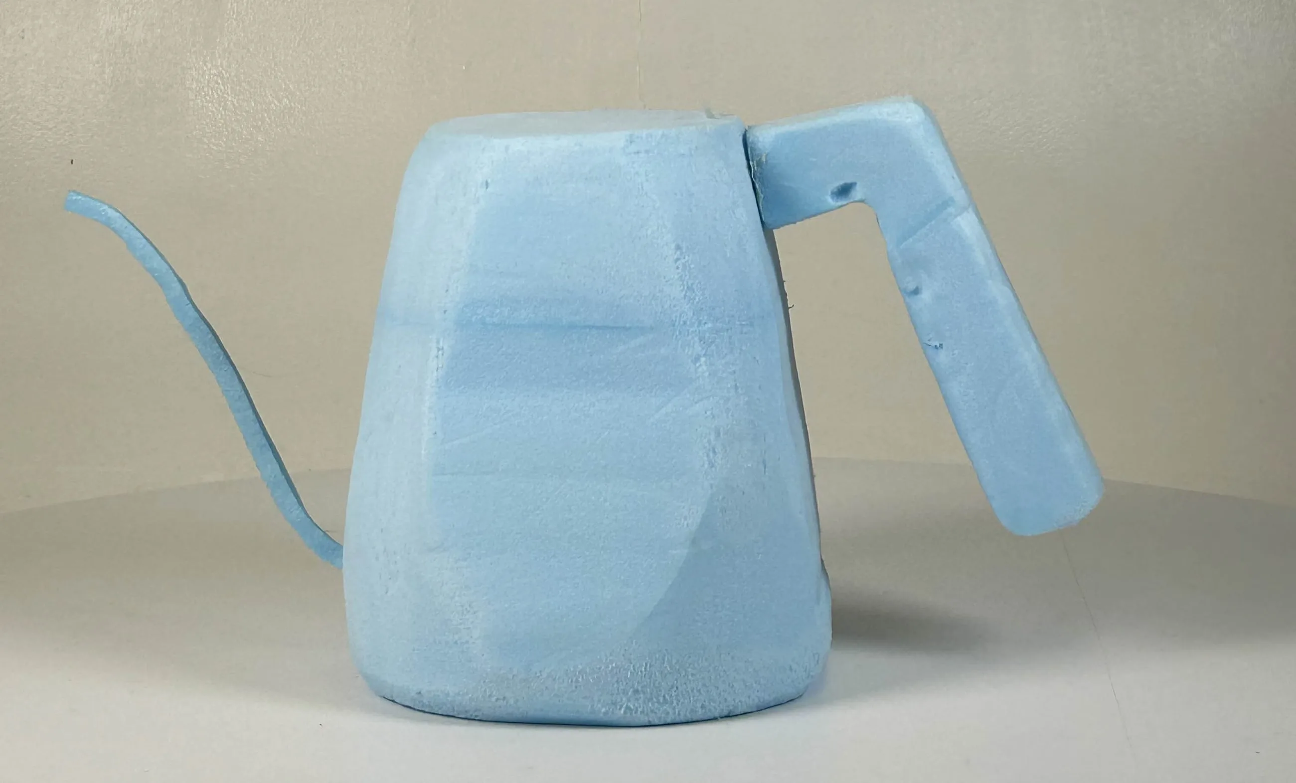 Rough blue foam model of the kettle, spout and straight handle carved as one block, seen side-on.