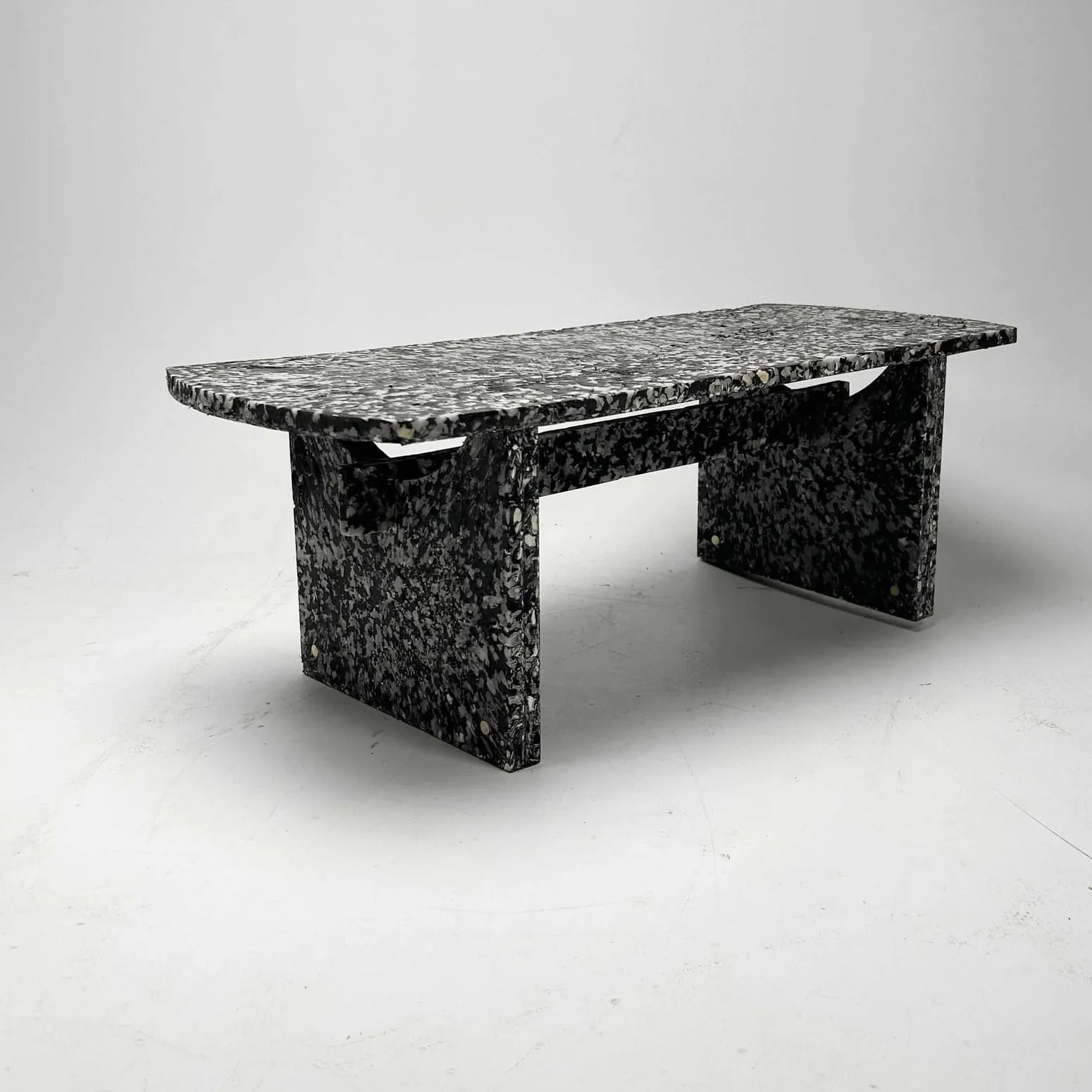 The finished bench in three-quarter view, brass fixings set into the speckled shell composite.