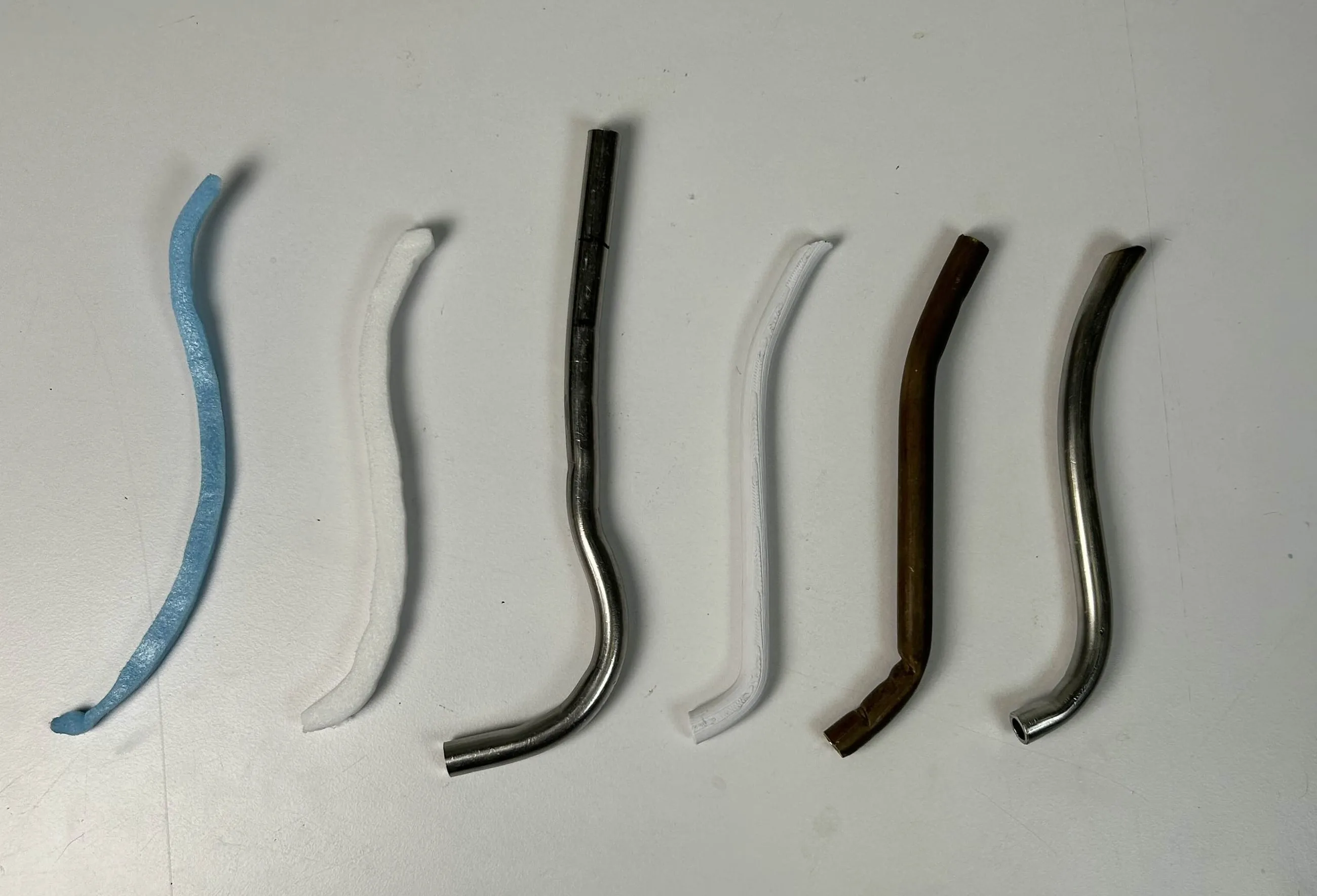 Six spout profiles laid out in a row: blue foam, two white prints, a brass tube and two bent steel tubes.